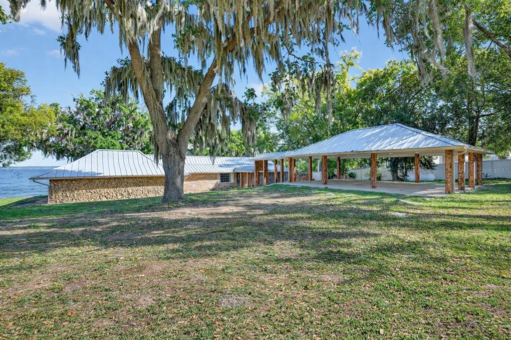 A stone-walled house with a metal roof and a large open-air pavilion near a lake — 13033 SE 158TH LANE, WEIRSDALE, FL
