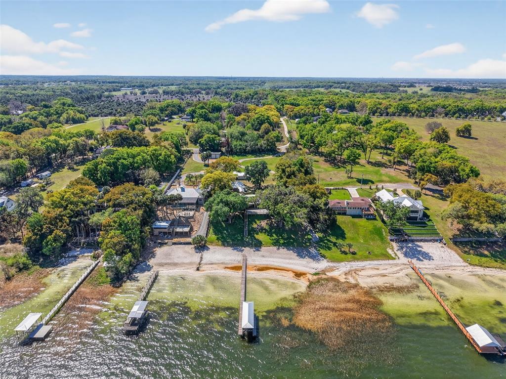 An aerial view shows three waterfront houses with private docks extending into a lake — 13033 SE 158TH LANE, WEIRSDALE, FL