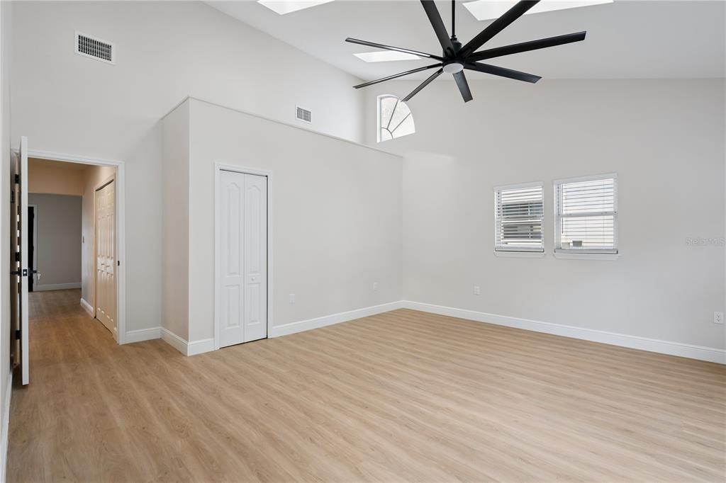 A bright, empty room features light wood-look flooring, a vaulted ceiling, and a large fan — 201 E MURIEL STREET, ORLANDO, FL