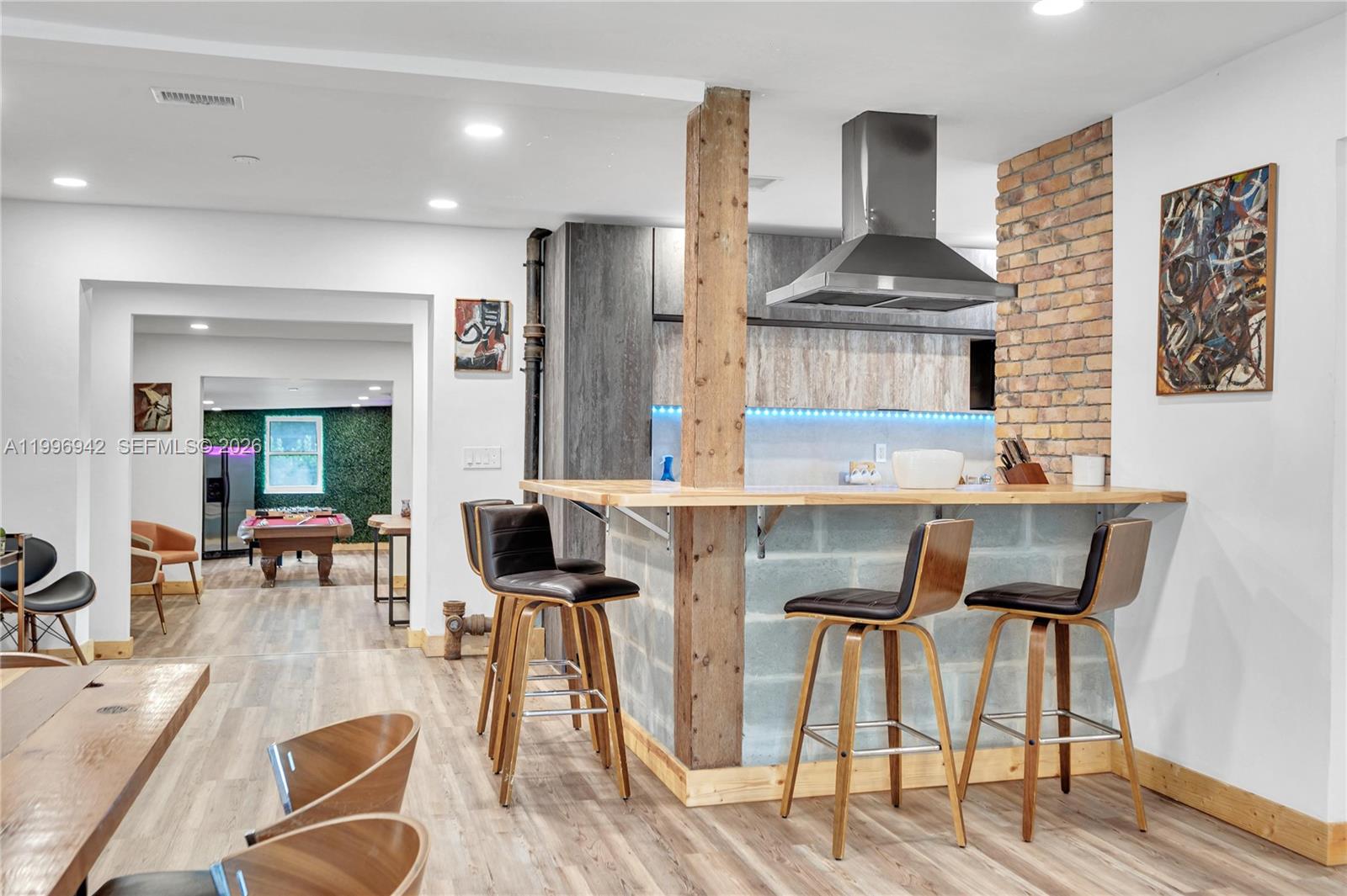 A kitchen features a wooden bar, brick accent wall, and stools overlooking a game room — 9000 NW 12th Ave, Miami FL 33150, MIAMI, FL