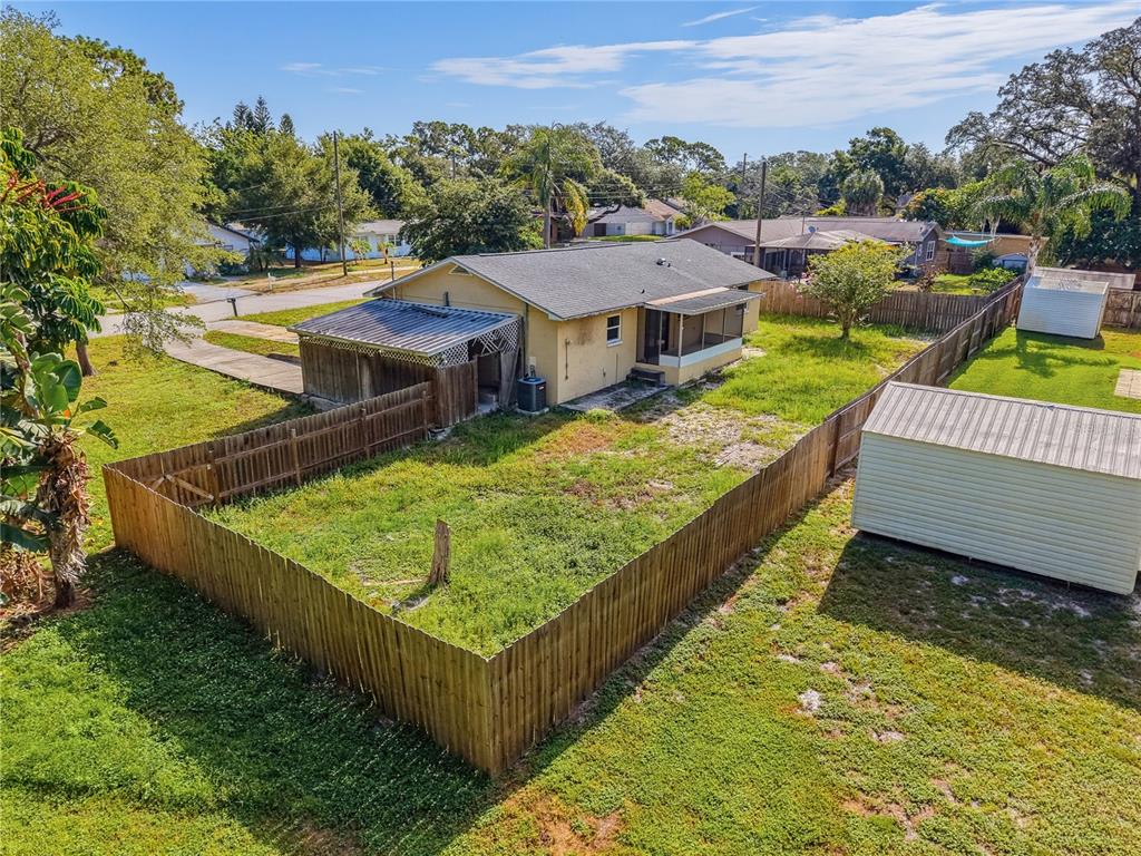 An aerial view shows a yellow house with a fenced backyard and two storage sheds — 1116 E OAKWOOD STREET, TARPON SPRINGS, FL