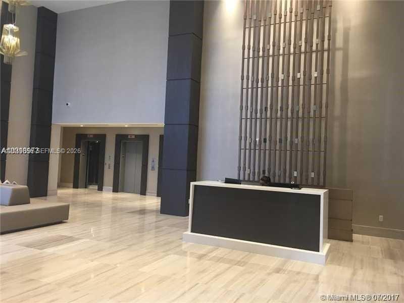 A modern lobby features a reception desk, tall decorative wall paneling, and marble flooring — 1010 SW 2nd Ave # 1105, Miami FL 33130, MIAMI, FL
