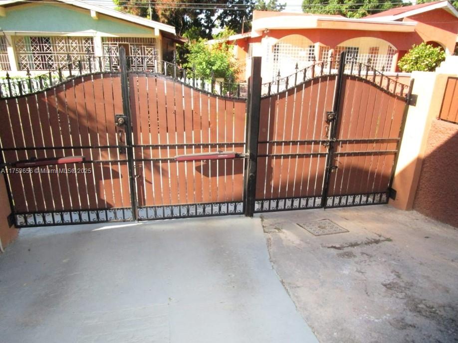 A driveway leads to a closed, arched metal and wood gate in front of two houses — 00 Queensbury, Kingston, Jamaica, NA, NA