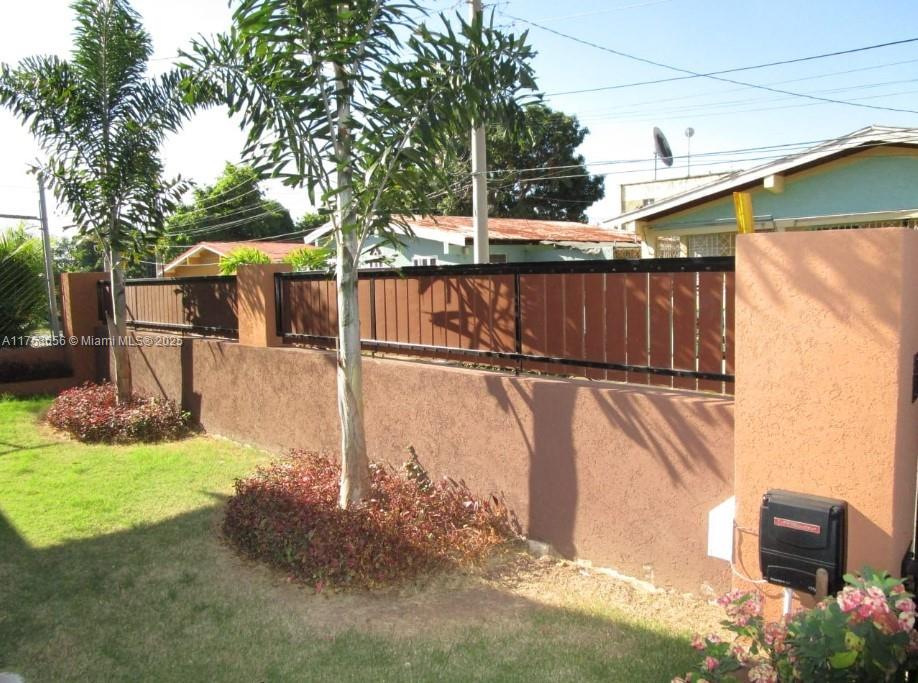 A brown stucco wall with a wood-slat fence sits in a grassy yard with trees — 00 Queensbury, Kingston, Jamaica, NA, NA