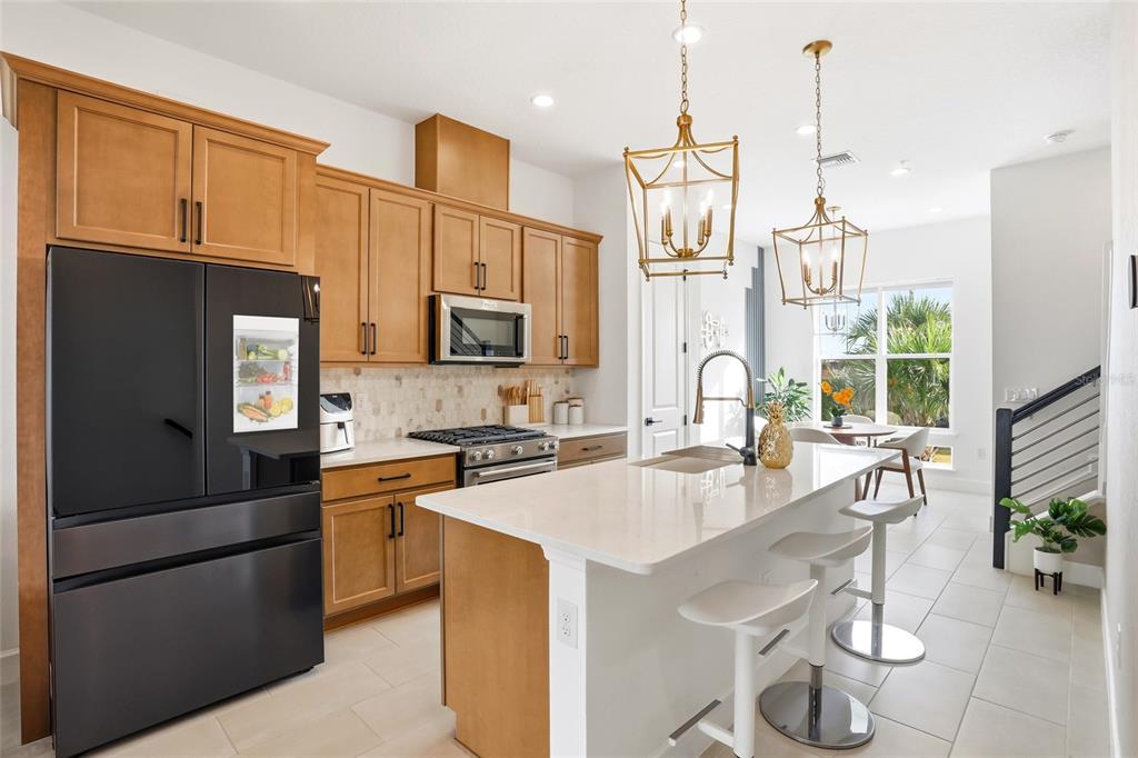 A modern kitchen features light wood cabinets, a black refrigerator, and a white quartz island — 2038 PACKING DISTRICT WAY, ORLANDO, FL