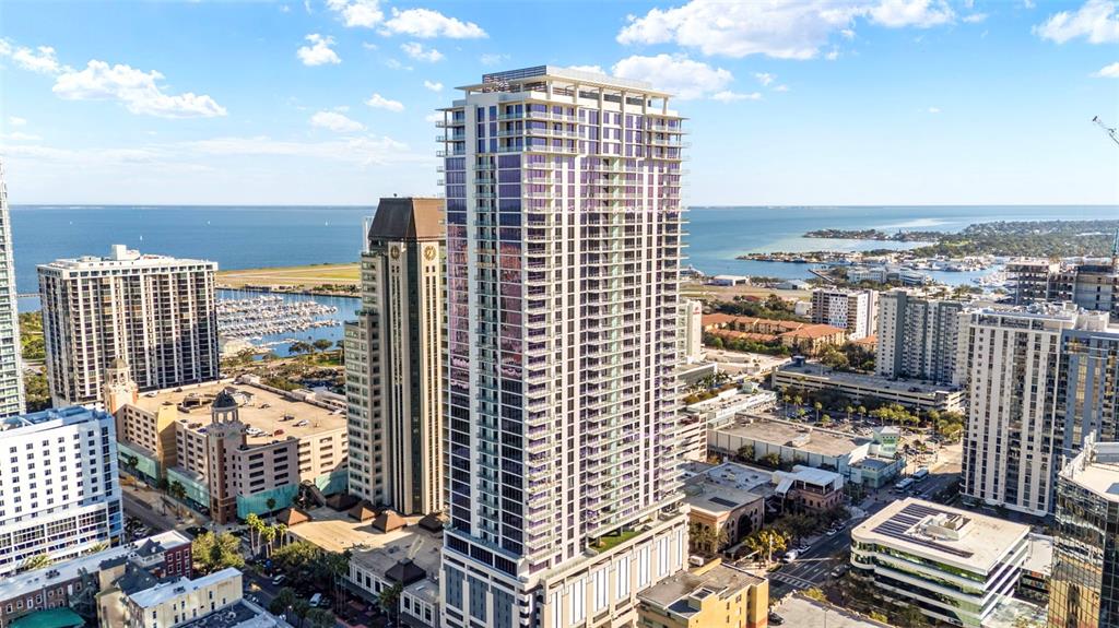 An aerial view shows a tall glass residential tower surrounded by other buildings and water — 275 1ST AVENUE S UNIT 2206, ST PETERSBURG, FL
