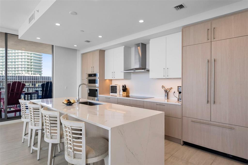 A modern kitchen features a white quartz island, light wood cabinetry, and a balcony view — 275 1ST AVENUE S UNIT 2206, ST PETERSBURG, FL