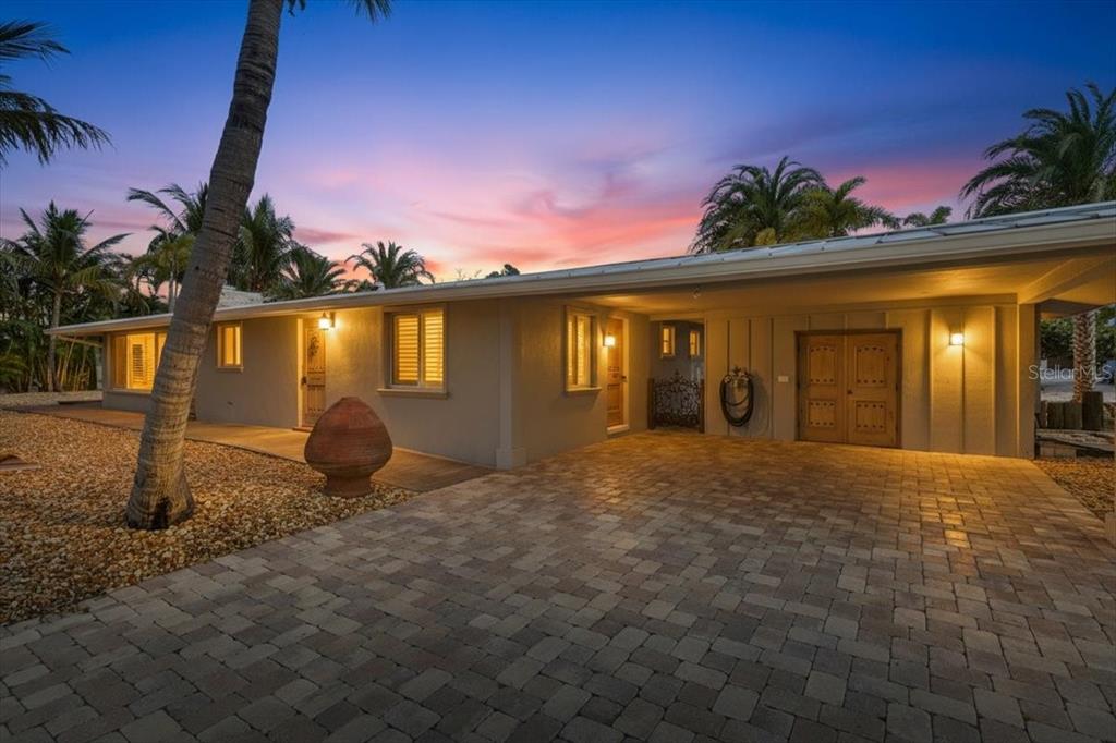 A single-story house with a paved driveway, covered entryway, and palm trees at sunset — 834 JUNGLE QUEEN WAY, LONGBOAT KEY, FL