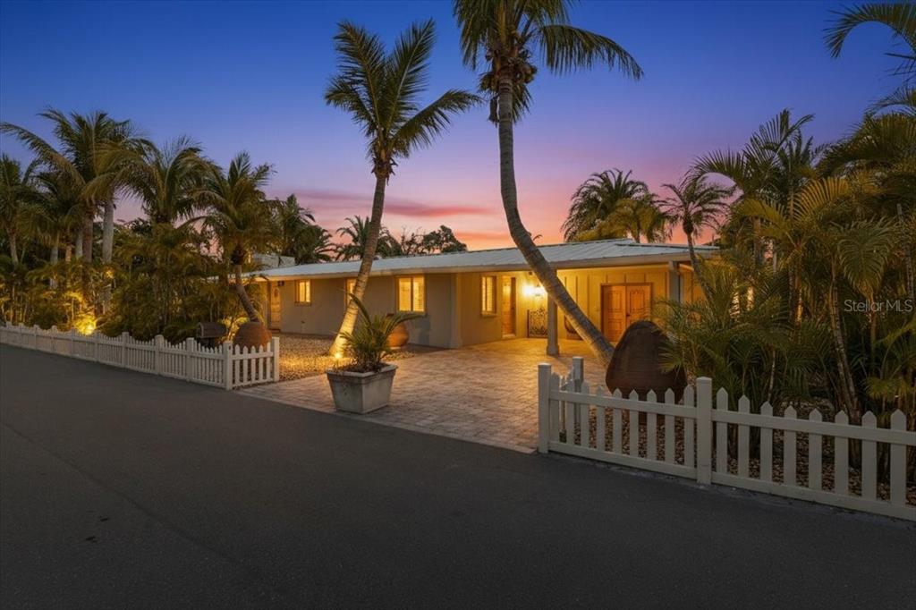 A single-story house with a paved driveway and palm trees at sunset behind a fence — 834 JUNGLE QUEEN WAY, LONGBOAT KEY, FL