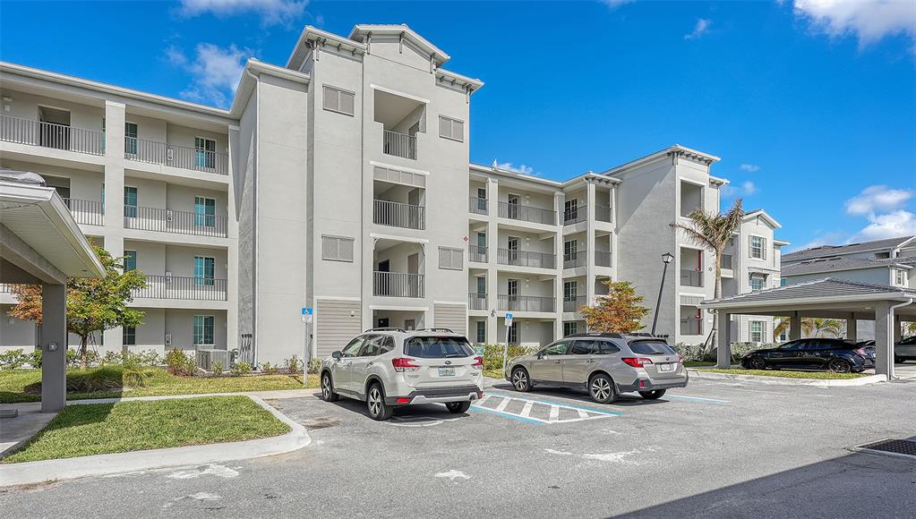 A multi-story apartment building with light-colored stucco walls and a parking lot in front — 12180 WELLEN GOLF STREET UNIT 202, VENICE, FL