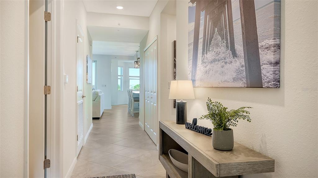 A hallway with tile flooring leads to an open living area featuring a console table — 12180 WELLEN GOLF STREET UNIT 202, VENICE, FL