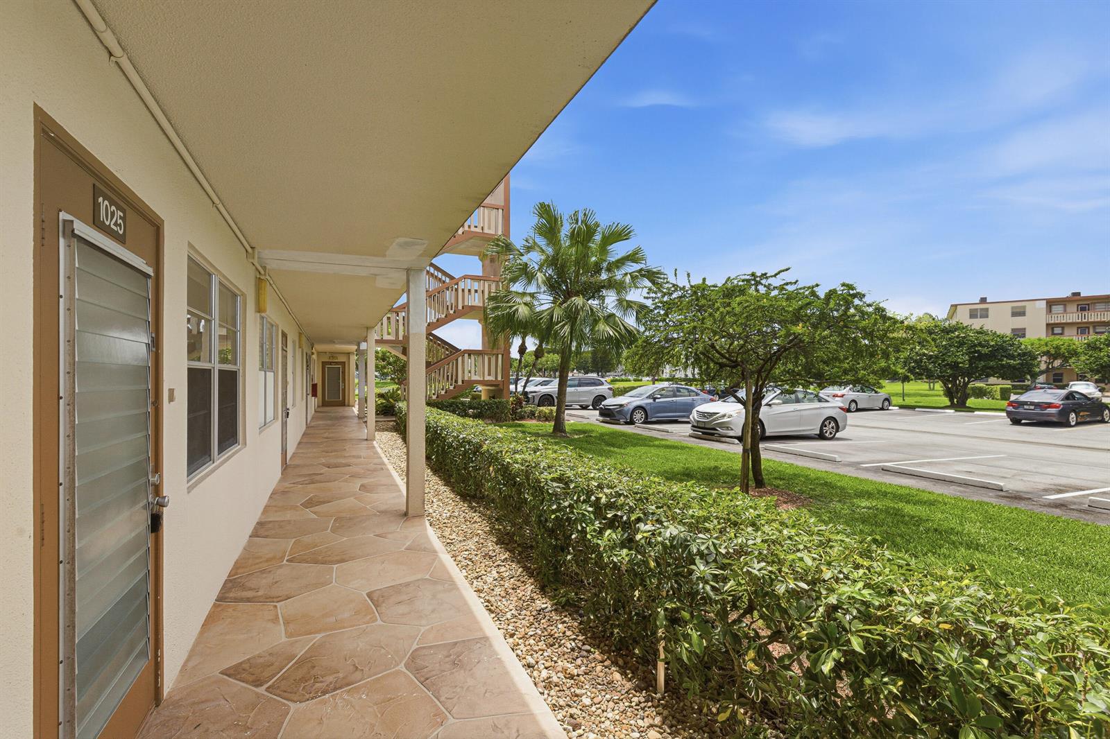 An outdoor walkway with tiled flooring leads past apartment doors toward a parking lot — 1025 Newcastle B # 1025, Boca Raton FL 33434, BOCA RATON, FL