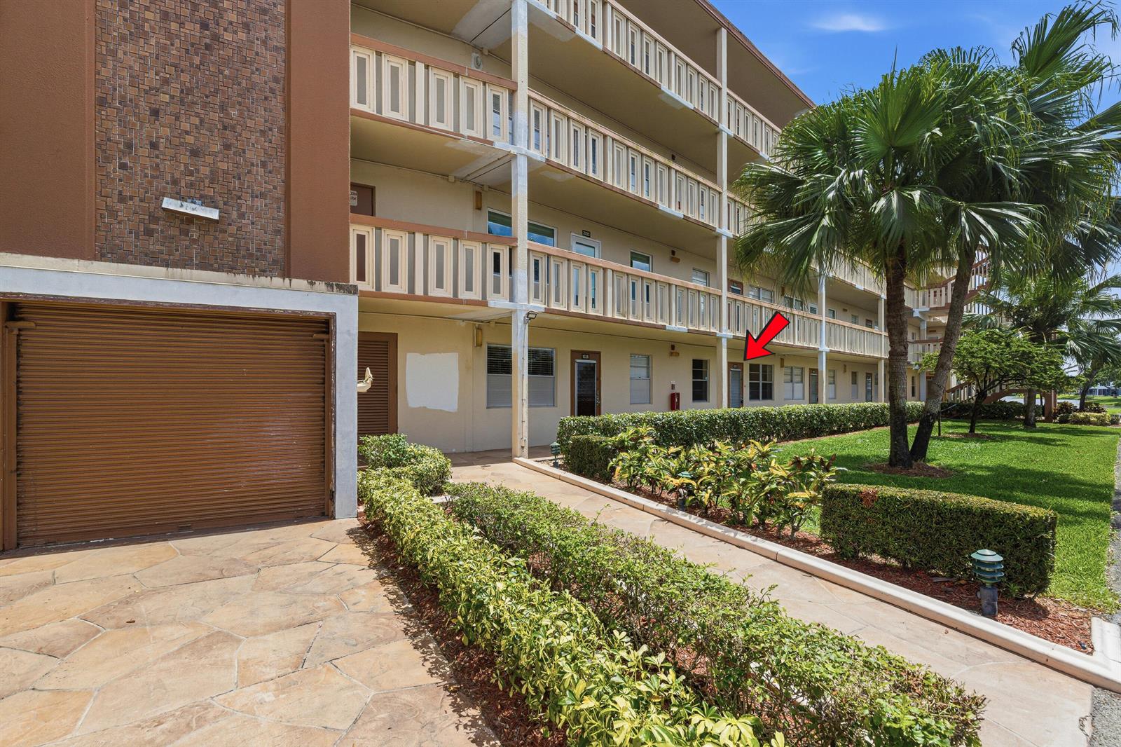 A ground-level view of a multi-story apartment building with a red arrow pointing to a unit — 1025 Newcastle B # 1025, Boca Raton FL 33434, BOCA RATON, FL