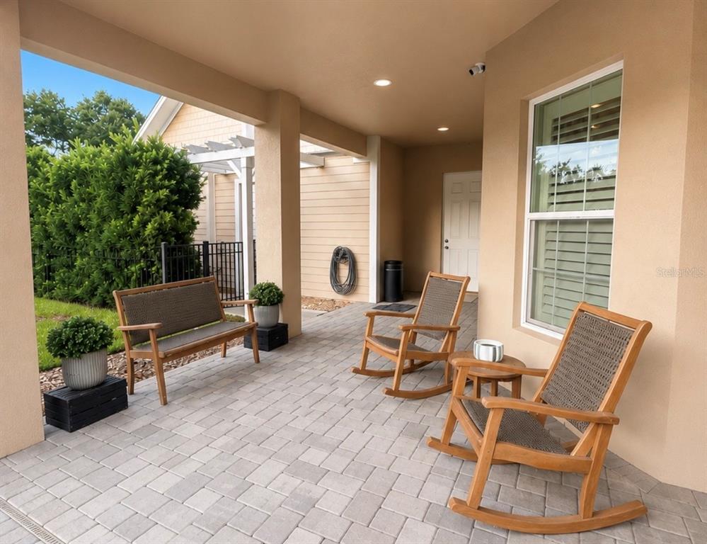 A covered patio features paver flooring, a bench, two rocking chairs, and a small table — 5650 KILLIANS PATH, WESLEY CHAPEL, FL