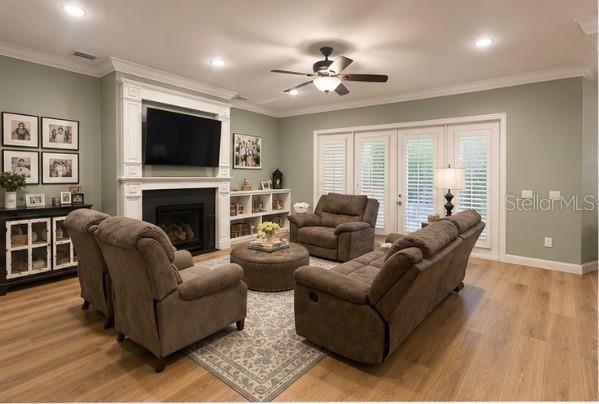 A living room features a fireplace, brown furniture, a ceiling fan, and light wood flooring — 5650 KILLIANS PATH, WESLEY CHAPEL, FL