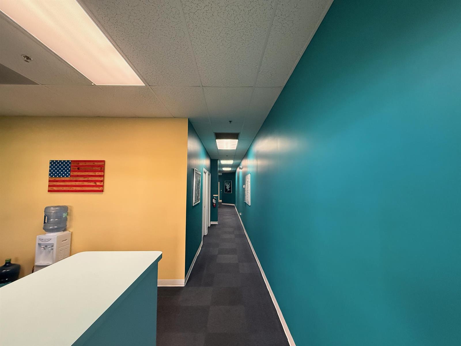 A hallway features teal walls on one side, a yellow wall with a flag, and carpeting — 6103 SE Federal Highway, Stuart FL 34997, STUART, FL