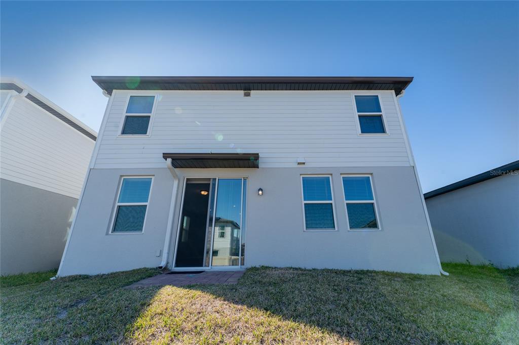 The rear exterior of a two-story house features white siding, stucco walls, and sliding doors — 3085 BELLA VISTA DRIVE, DAVENPORT, FL