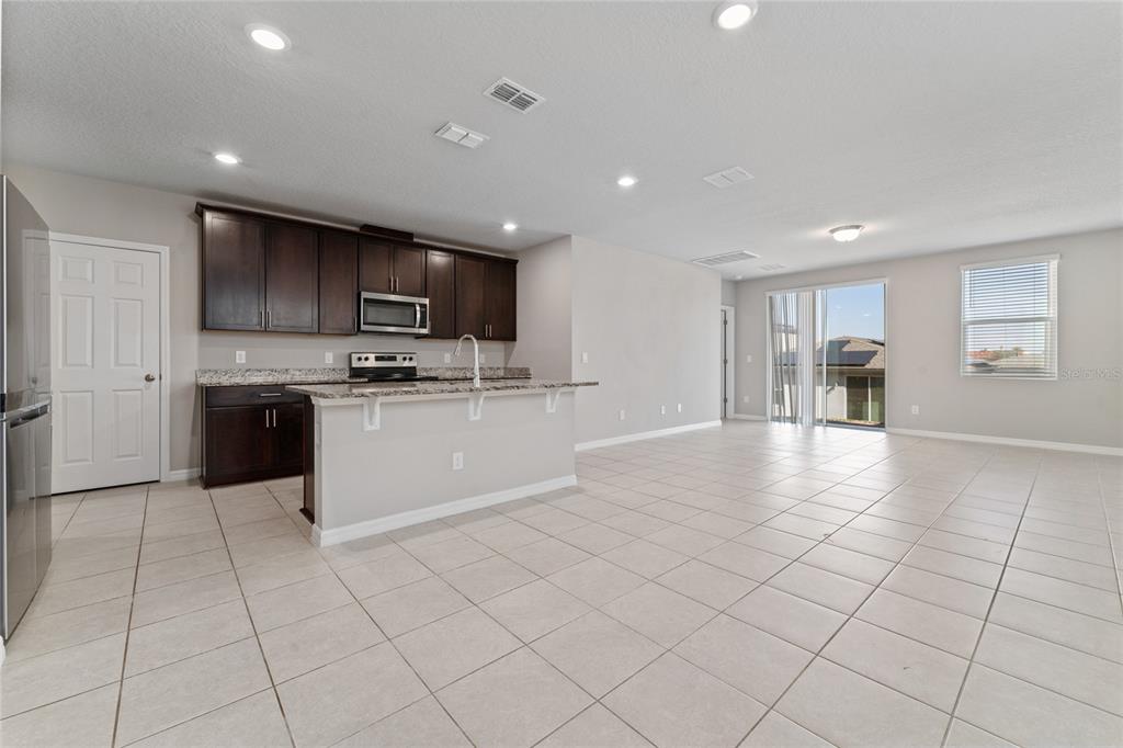A kitchen with dark cabinets and granite countertops opens into a large tiled living area — 3085 BELLA VISTA DRIVE, DAVENPORT, FL