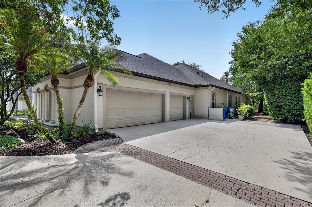 A side view of a house exterior featuring a three-car garage and a concrete driveway — 6353 W MACLAURIN DRIVE, TAMPA, FL