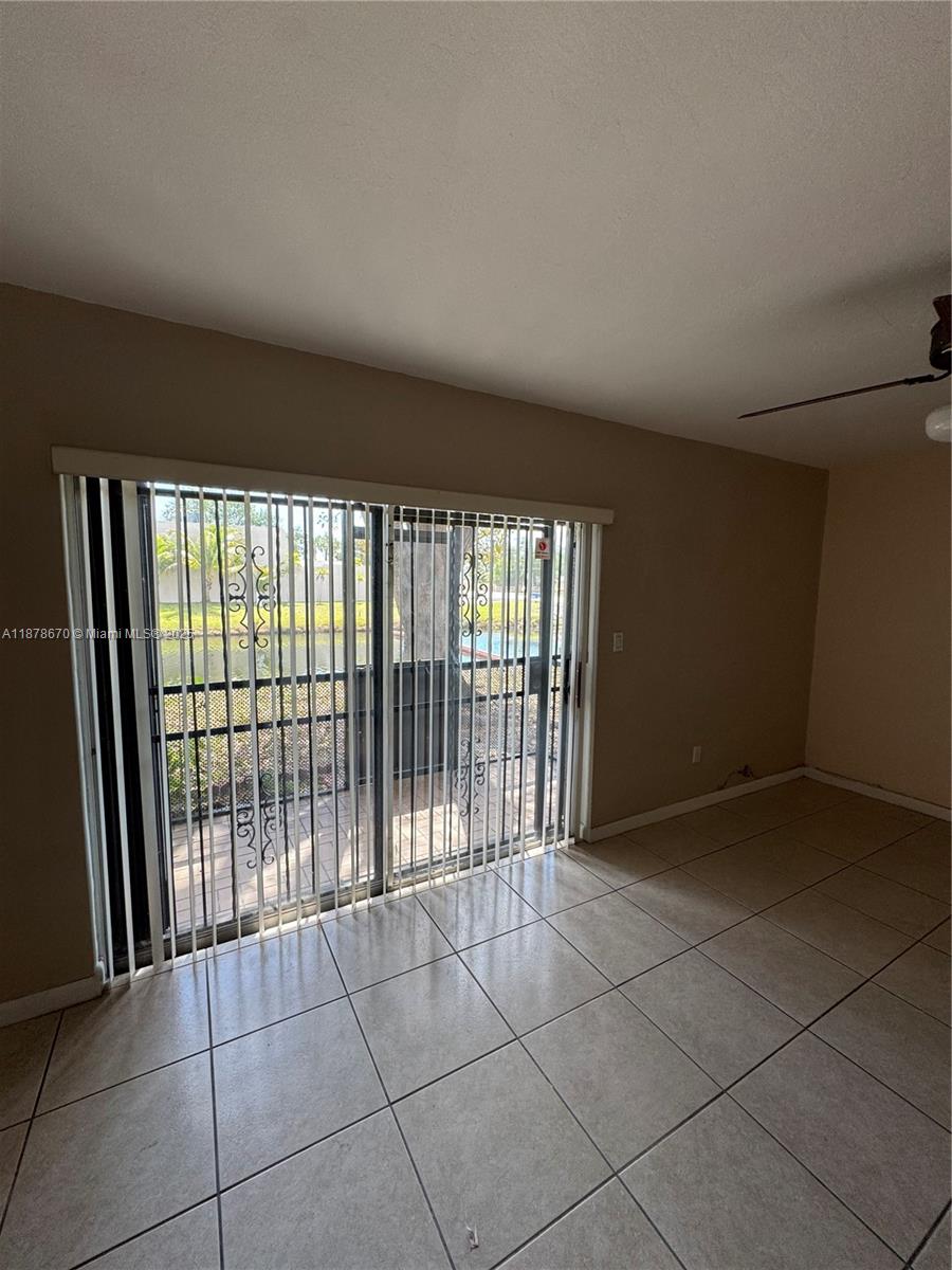 An empty room with light-colored tile flooring and sliding glass doors leading to a patio — 10353 N Kendall Dr, Miami FL 33176, MIAMI, FL