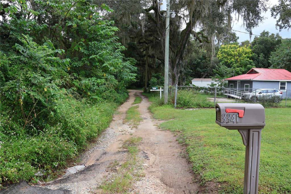 A dirt driveway leads past a mailbox toward a house with a red metal roof — 3330 SE 11TH AVENUE, OCALA, FL