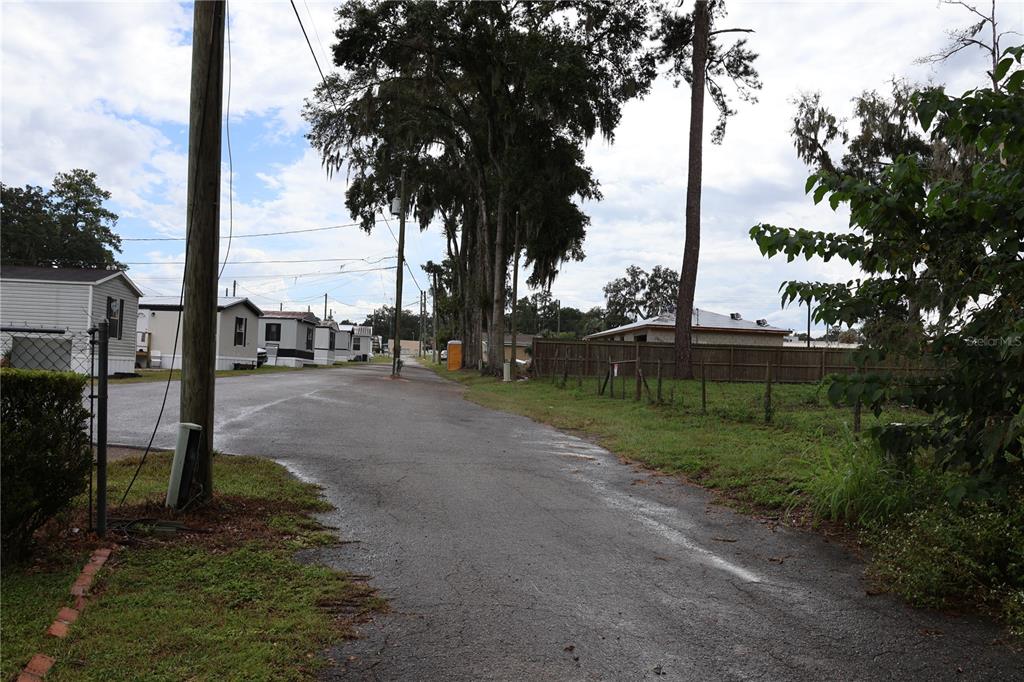 A paved road leads past mobile homes toward a wooden fence and tall trees — 3330 SE 11TH AVENUE, OCALA, FL
