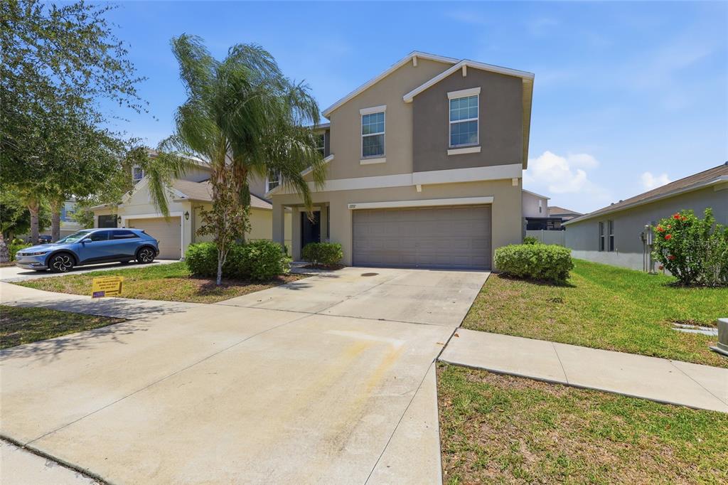 A two-story suburban house features a beige stucco exterior, a two-car garage, and a driveway — 17237 WHITE MANGROVE DRIVE, WIMAUMA, FL