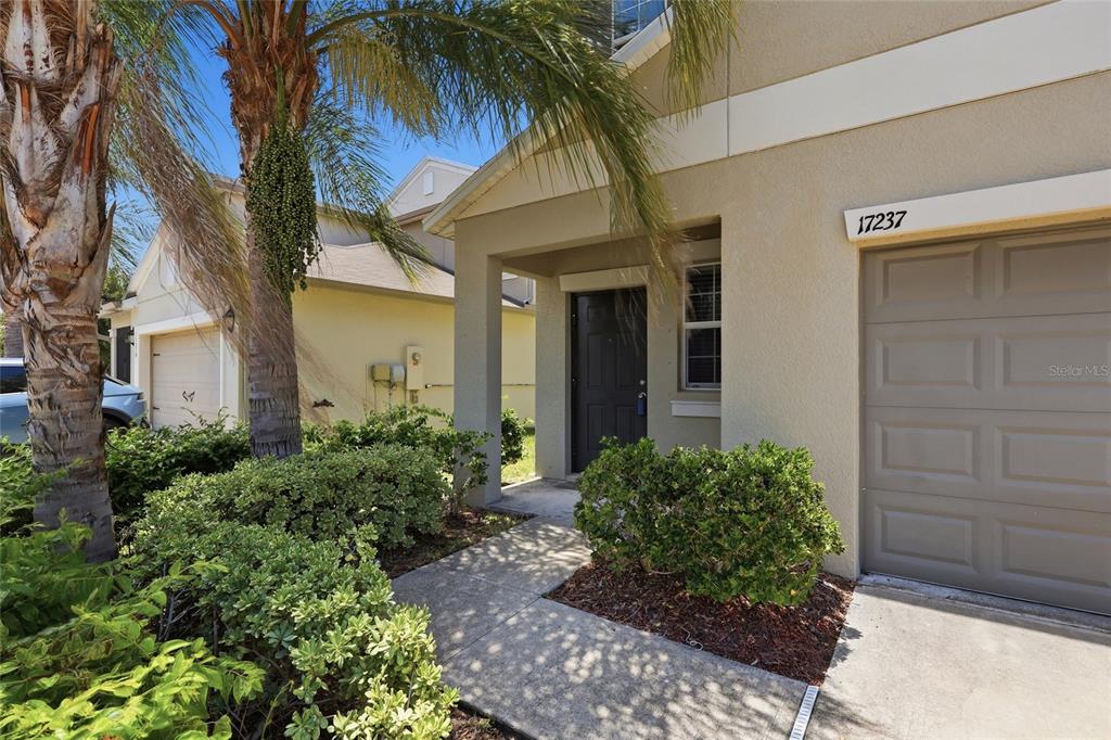 A beige house exterior features a covered entryway, a dark front door, and a garage — 17237 WHITE MANGROVE DRIVE, WIMAUMA, FL
