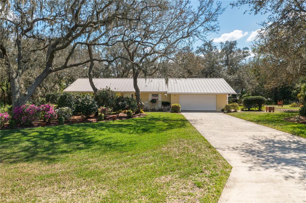 A single-story yellow house with a metal roof and a concrete driveway sits among trees — 41 SPRING LANE, HAINES CITY, FL