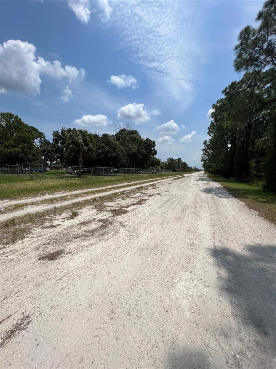 A dirt road runs alongside a fenced property with trees under a blue sky — 681 N Perimeter Road, Clewiston FL 33440, CLEWISTON, FL