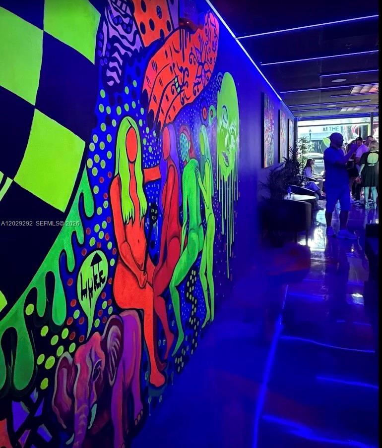A hallway features a vibrant, neon-colored mural on one wall under blue accent lighting — MIAMI BEACH, FL