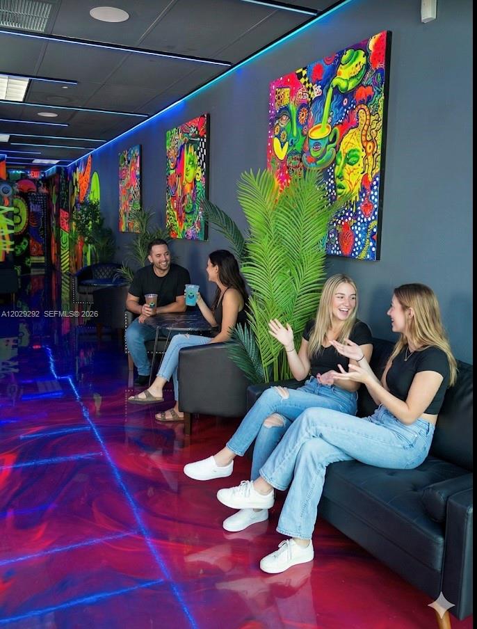 A lounge area features colorful wall art, a glossy red floor, and four people seated — MIAMI BEACH, FL
