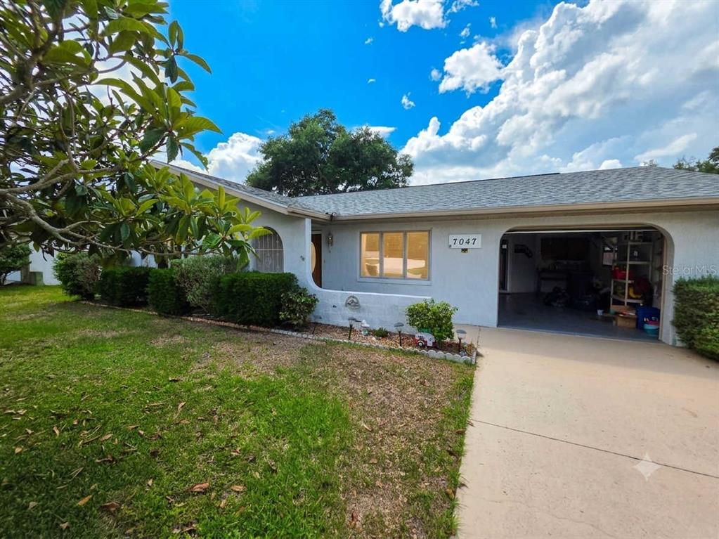 A single-story house with a light-colored exterior, a garage, and a front lawn — 7047 WINDMERE ROAD, BROOKSVILLE, FL
