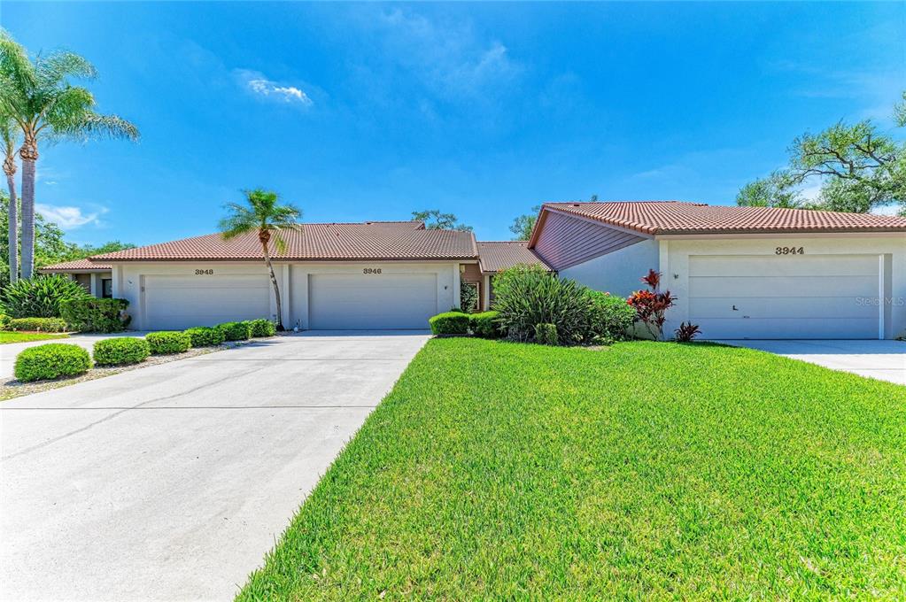 A view of the exterior of three attached residential units with garages and a lawn — 3946 WILSHIRE CIRCLE E UNIT 168, SARASOTA, FL