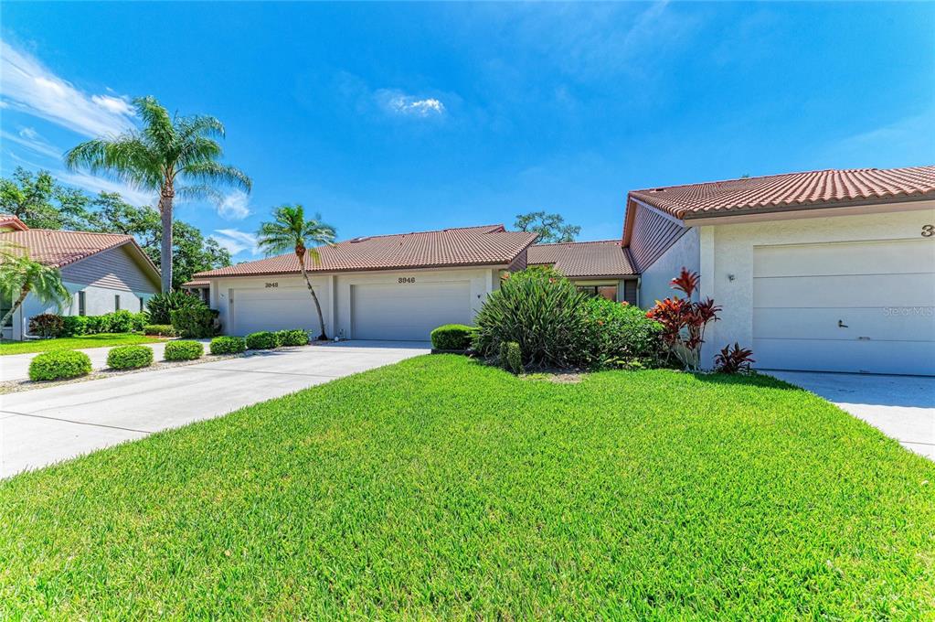 A row of attached single-story homes with tiled roofs and attached garages under a blue sky — 3946 WILSHIRE CIRCLE E UNIT 168, SARASOTA, FL
