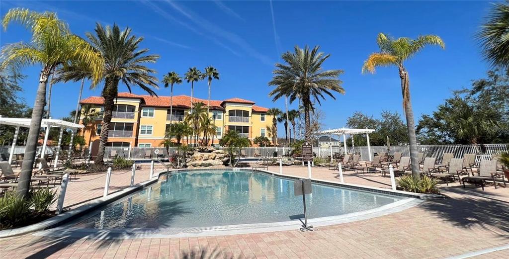 A swimming pool with a rock water feature is surrounded by palm trees and buildings — 5479 VINELAND ROAD UNIT 9213, ORLANDO, FL