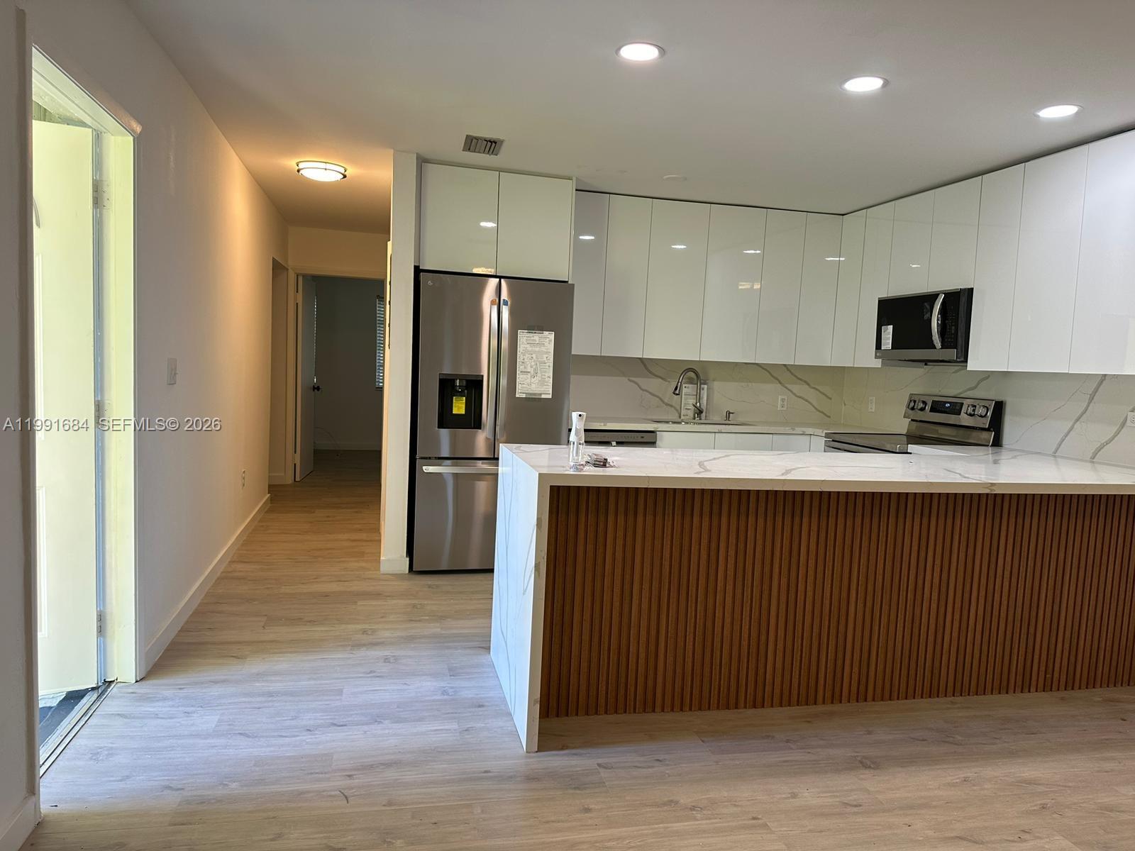 A modern kitchen features white glossy cabinets, a marble-patterned island, and light wood flooring — 3755 Oak Ave, Miami FL 33133, MIAMI, FL