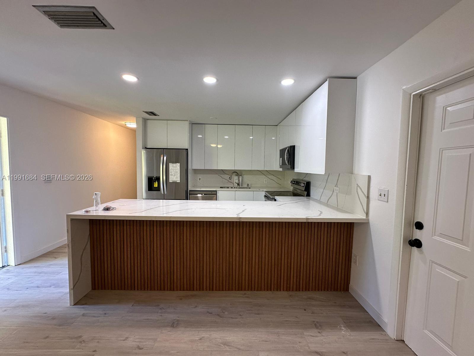 A modern kitchen features white glossy cabinets, a marble-patterned countertop, and a slatted wood island — 3755 Oak Ave, Miami FL 33133, MIAMI, FL