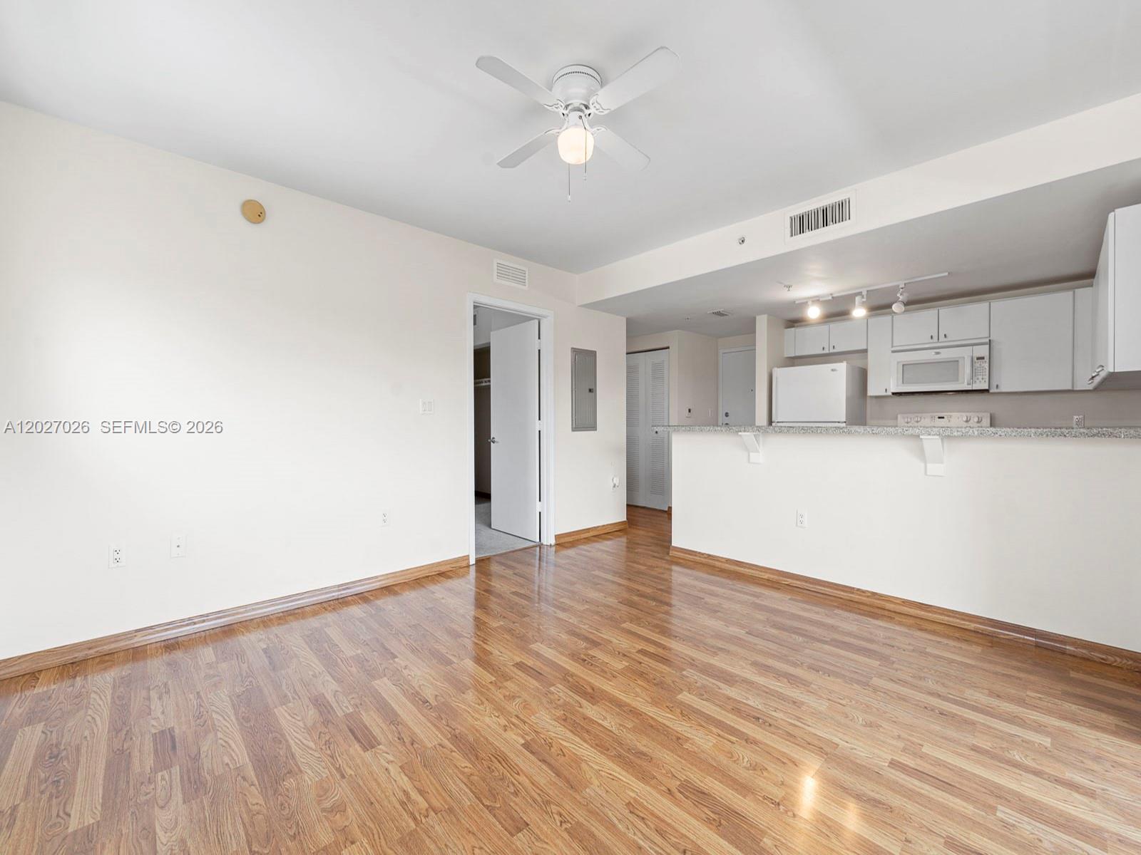An empty room features hardwood floors, a ceiling fan, and an open kitchen with white cabinets — 2740 SW 28th Ter # 508, Miami FL 33133, MIAMI, FL
