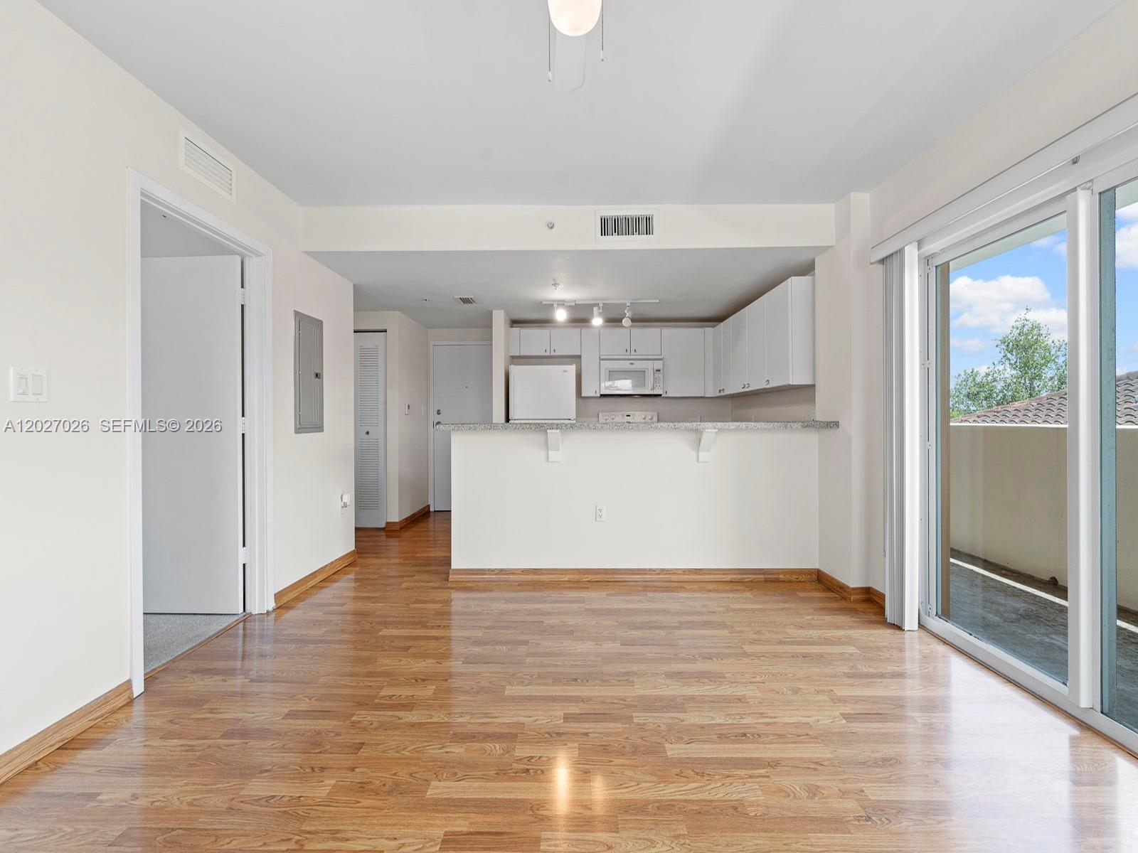 An open-concept living area features wood-look flooring, a kitchen with white cabinets, and a balcony — 2740 SW 28th Ter # 508, Miami FL 33133, MIAMI, FL