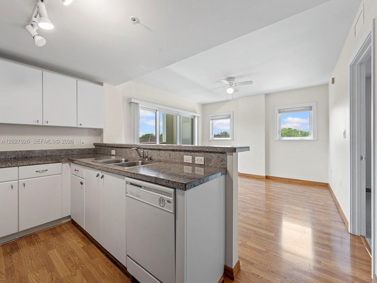 A kitchen with white cabinets and granite countertops opens to a living area with windows — 2740 SW 28th Ter # 508, Miami FL 33133, MIAMI, FL