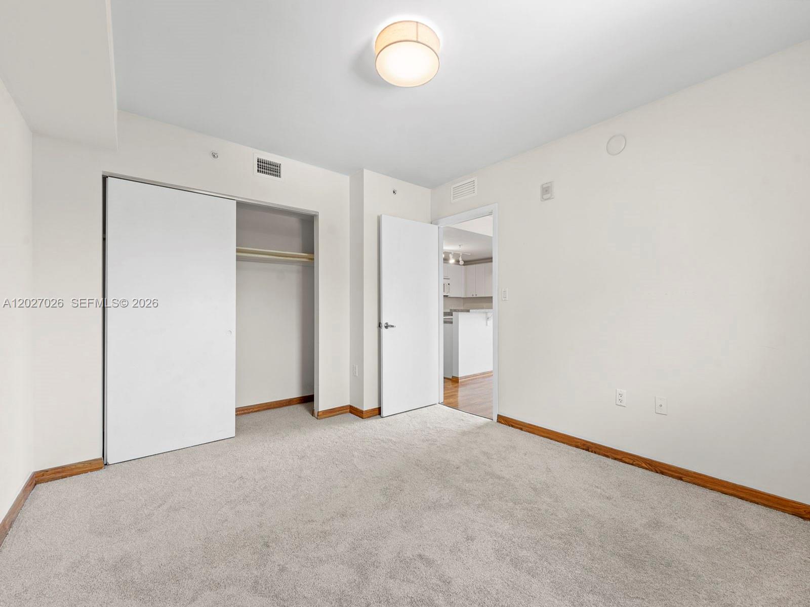 A bedroom with white walls, beige carpeting, a sliding closet door, and a doorway — 2740 SW 28th Ter # 508, Miami FL 33133, MIAMI, FL
