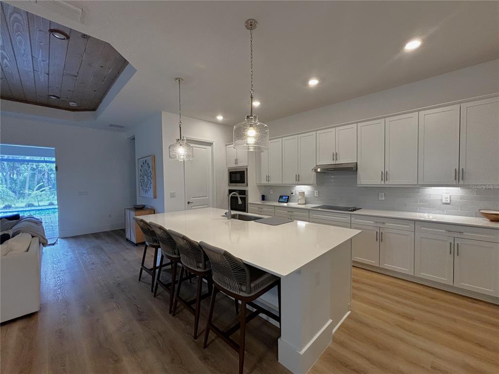 A modern kitchen features white cabinetry, a large quartz island with seating, and wood flooring — 17435 JADESTONE COURT, VENICE, FL