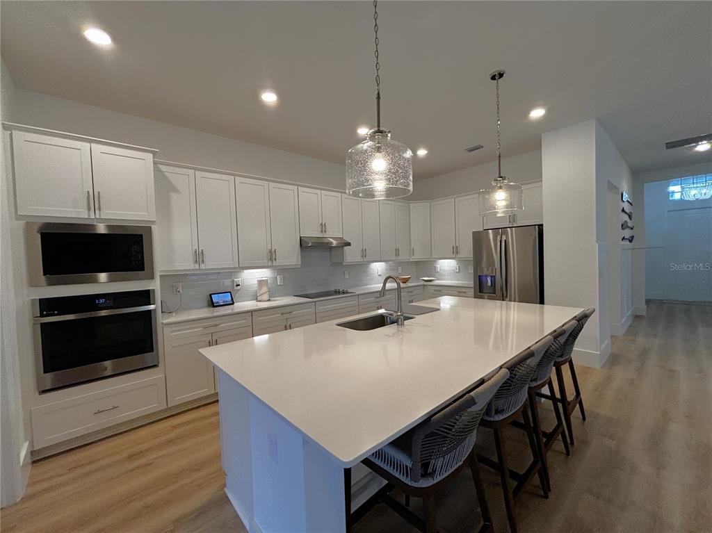 A modern kitchen features white cabinetry, a large quartz island, and stainless steel appliances — 17435 JADESTONE COURT, VENICE, FL