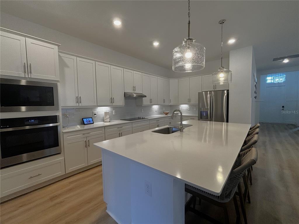 A modern kitchen features white cabinetry, a large quartz island, and stainless steel appliances — 17435 JADESTONE COURT, VENICE, FL