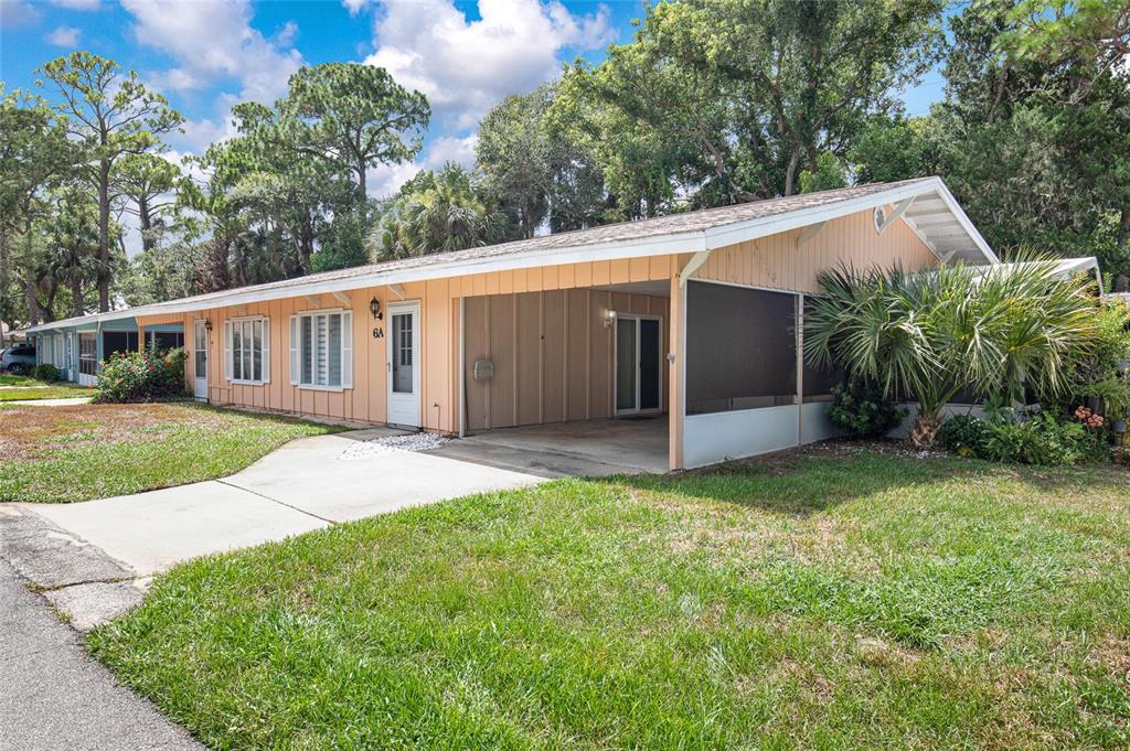 A single-story peach-colored house features a concrete driveway, a carport, and a screened-in porch — 6 COUNTRY CLUB DRIVE UNIT 6A, NEW SMYRNA BEACH, FL
