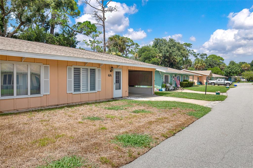 A single-story peach-colored house with a carport and a front lawn under a blue sky — 6 COUNTRY CLUB DRIVE UNIT 6A, NEW SMYRNA BEACH, FL