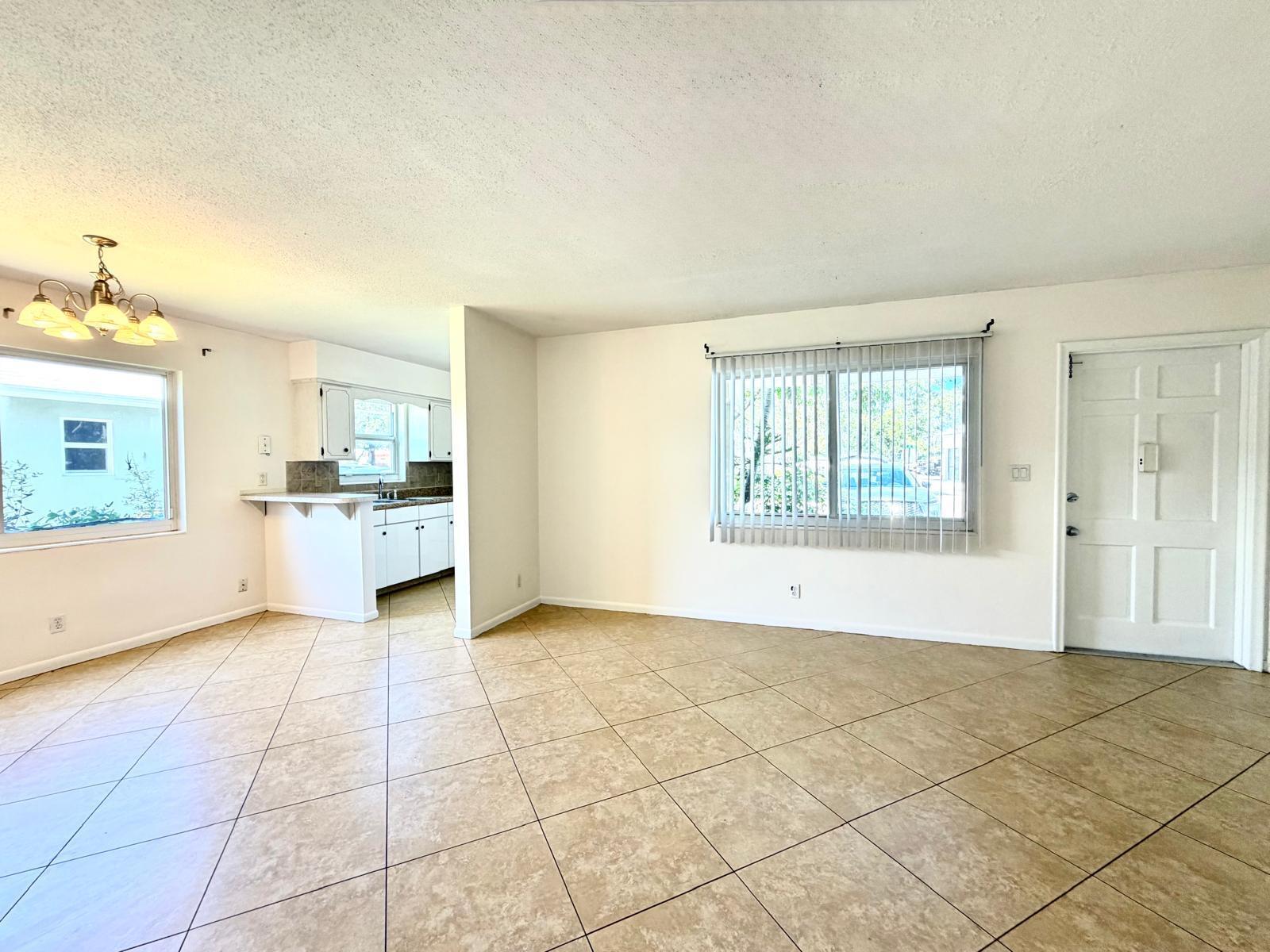An open-concept living area features beige tile flooring, white walls, a kitchen pass-through, and windows — 4731 NE 21st Terrace # 2, Lighthouse Point FL 33064, LIGHTHOUSE POINT, FL