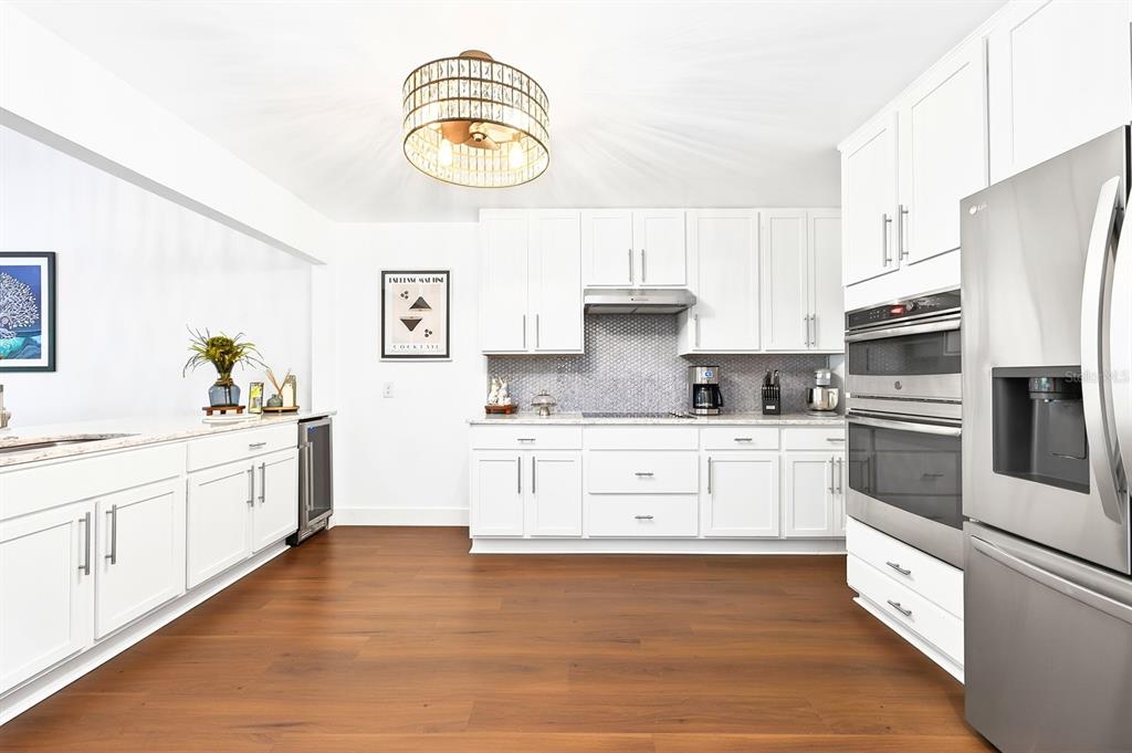 A kitchen features white cabinets, stainless steel appliances, a gray tile backsplash, and wood flooring — 314 SAND TRAP COVE, LONGWOOD, FL