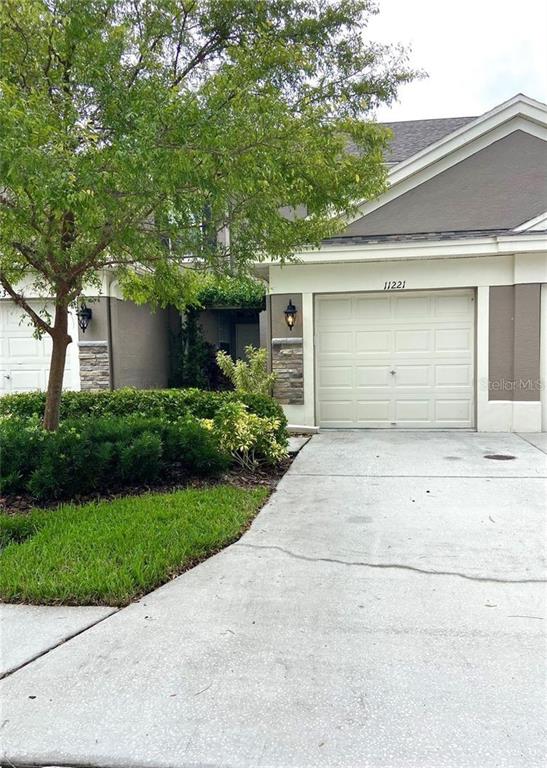 A single-story residential building features a beige garage, stone accents, and a front yard tree — 11221 WINDSOR PLACE CIRCLE, TAMPA, FL